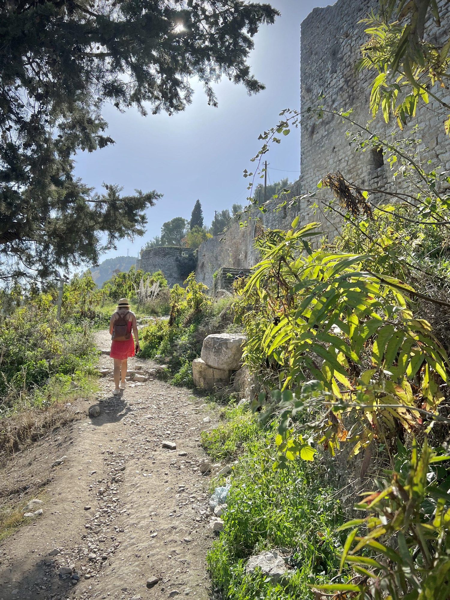 A cobbled lane between stone walls inside a castle, with houses and greenery and a woman walking ahead.