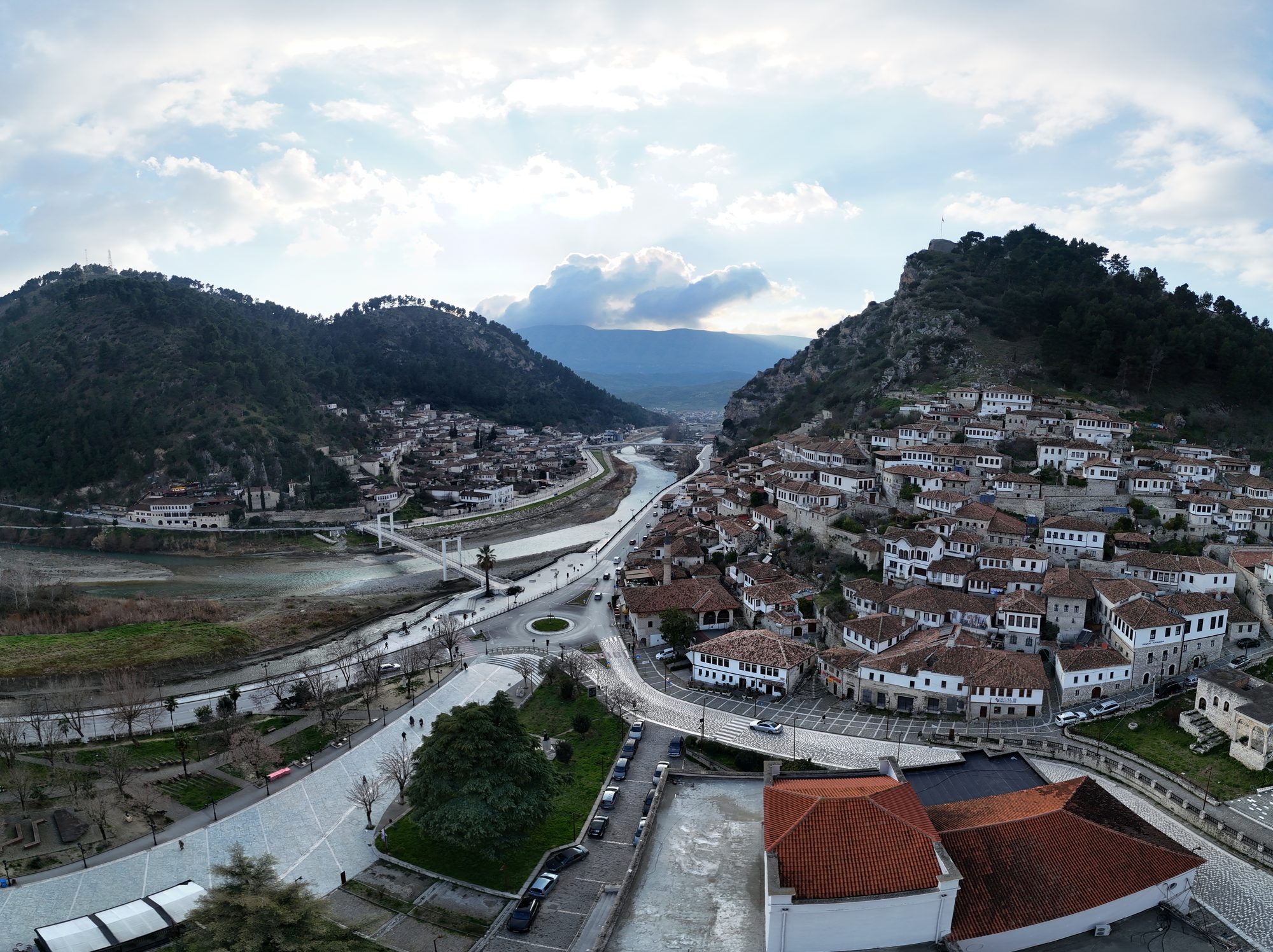 Tiers of white Ottoman houses with many windows climbing a steep hillside above a river, castle walls at the top.