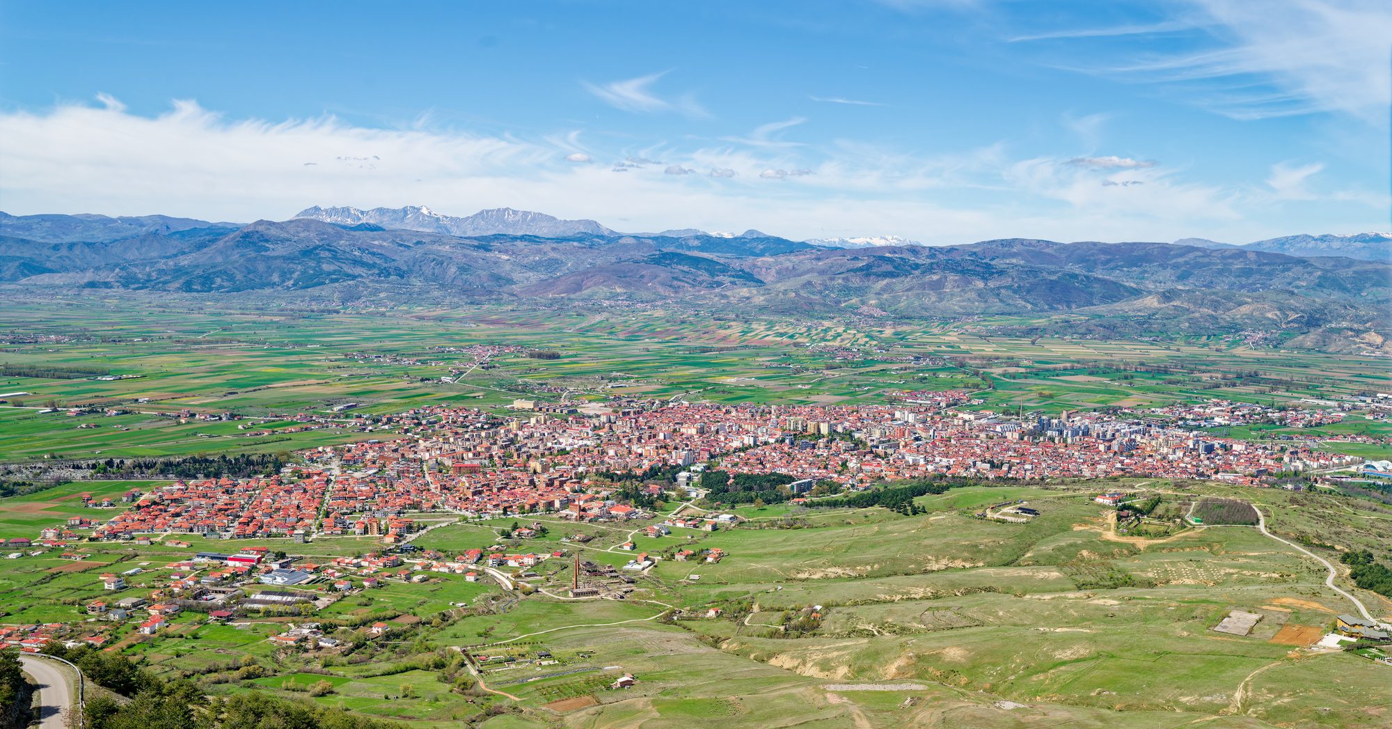 Wide view over the city of Korçë spread across a flat plain, seen from a mountain viewpoint, with hills on the far side of the valley.