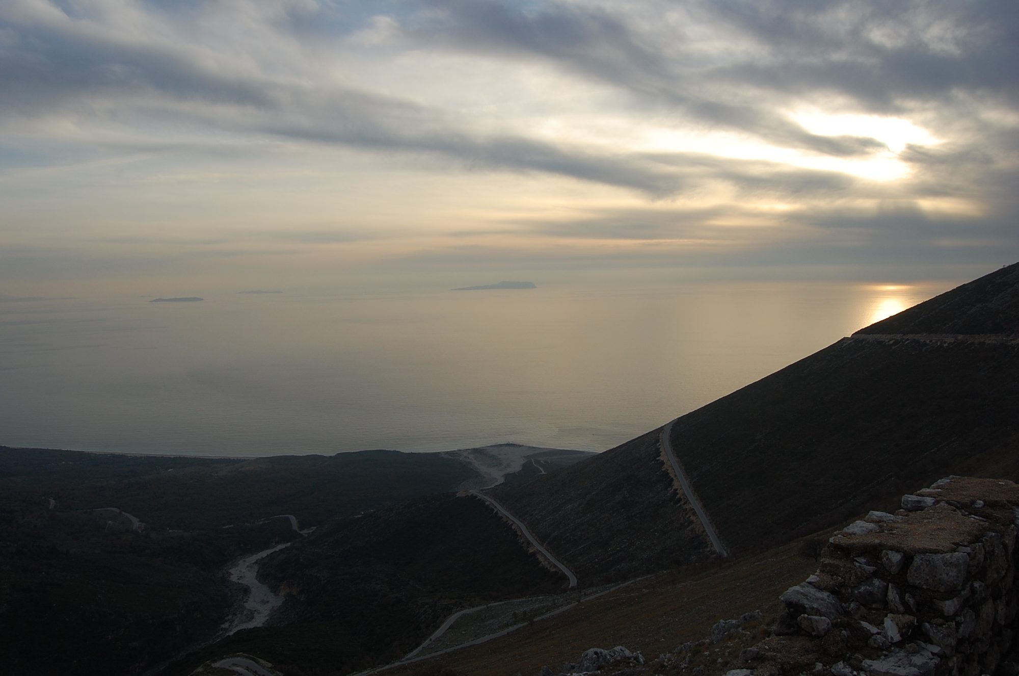 A view from a high mountain pass down over forested slopes to the sea, with islands visible on the horizon.
