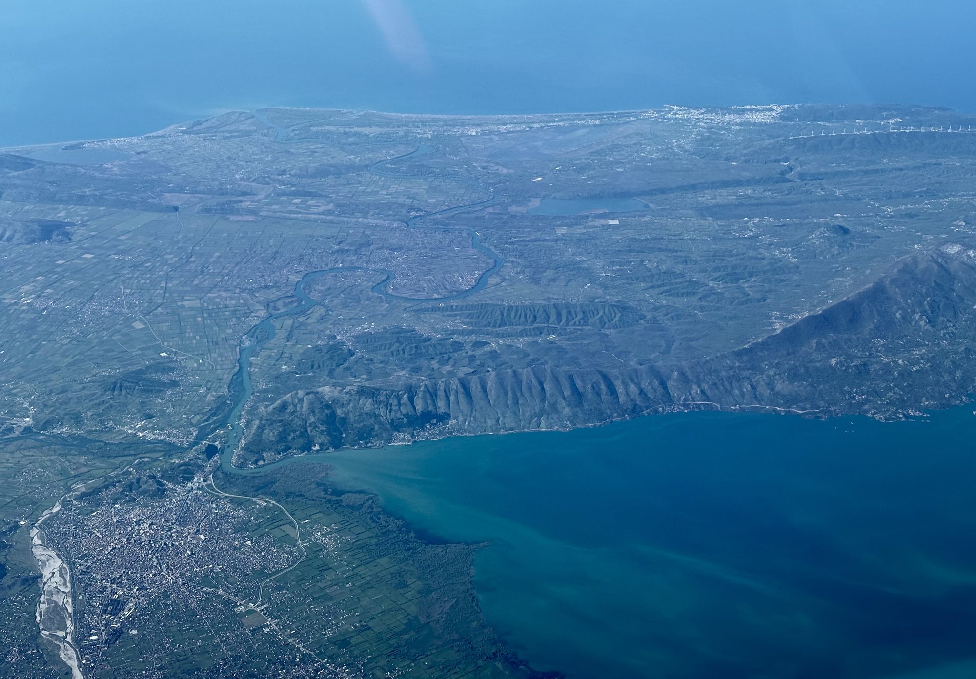 Aerial view from an aircraft of a large lake with a city on its shore, mountains rising on the far side and haze over the plain.