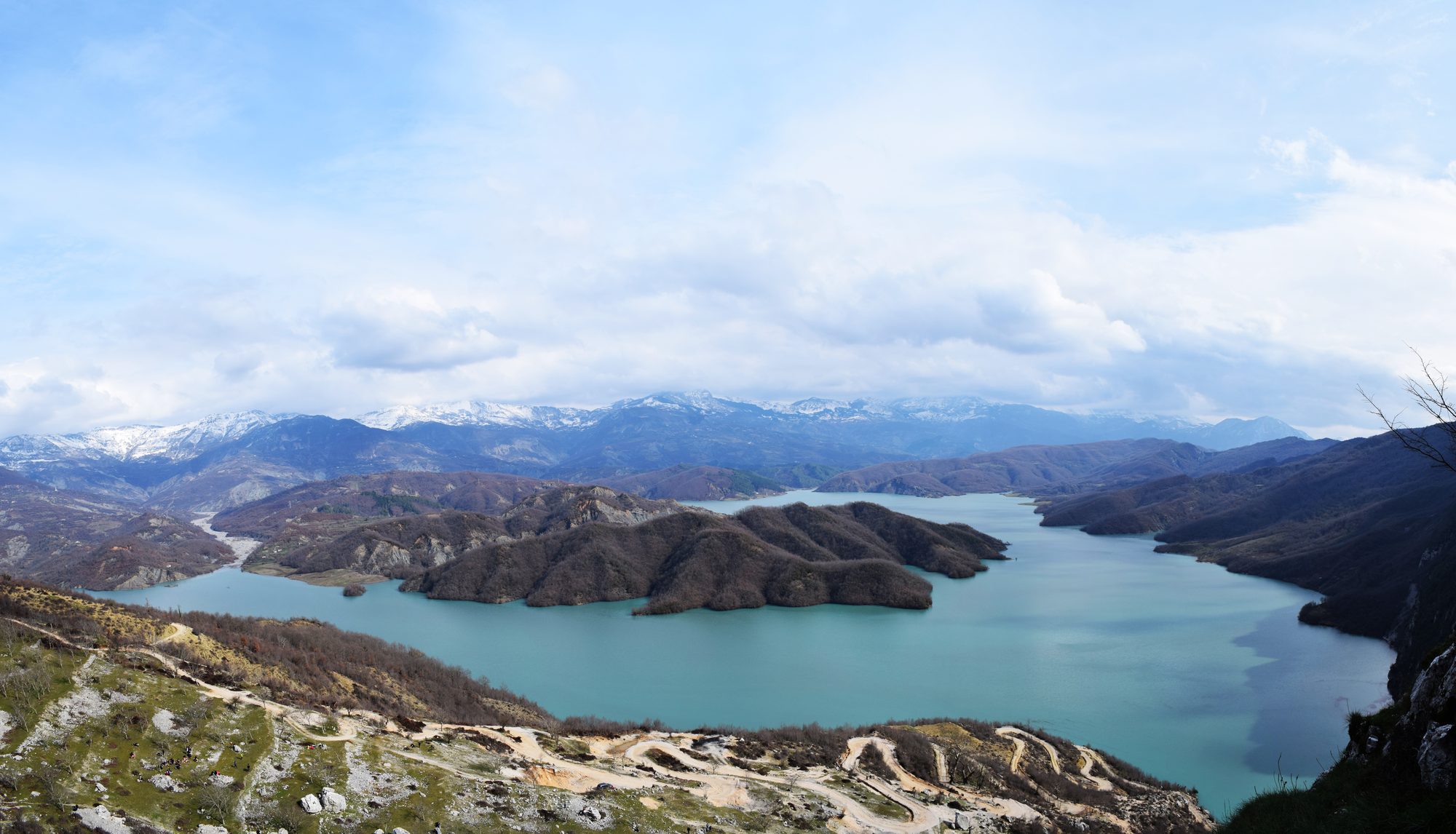 A narrow turquoise reservoir winding between steep pale limestone ridges under a clear sky.