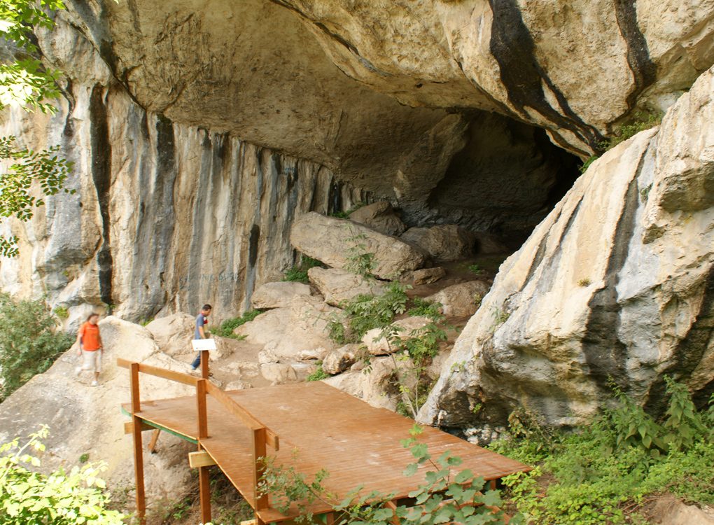 A wide dark cave mouth in a rocky hillside, with a rough path leading up to the entrance.