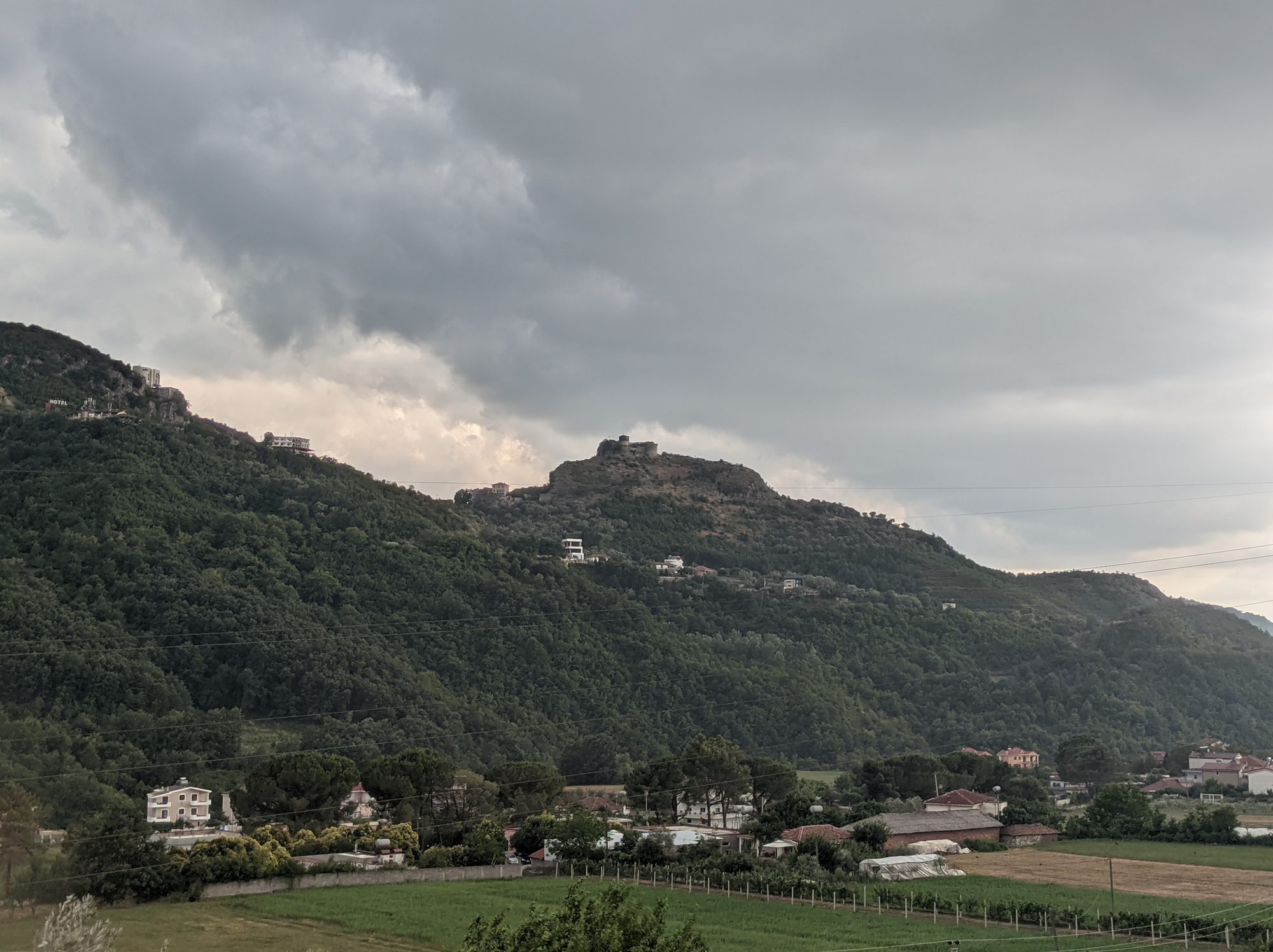 A compact stone castle with a round tower on a wooded hilltop above a green valley.