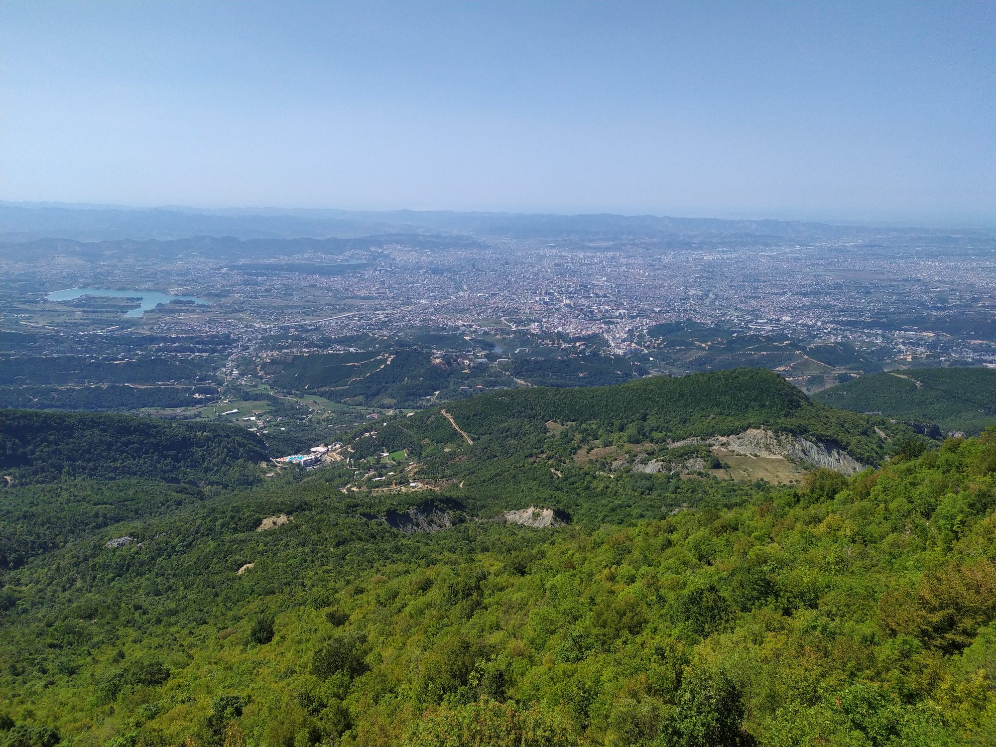 The city of Tirana spread across a wide plain, seen from a high grassy slope on Mount Dajti.