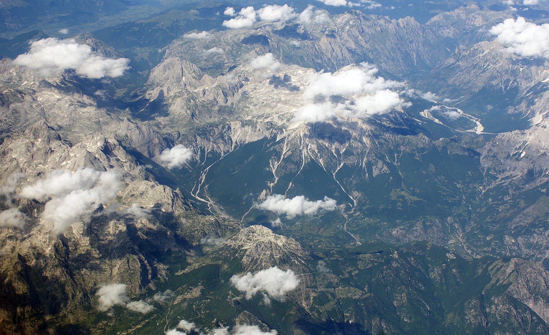 Aerial view of steep grey limestone peaks and deep green valleys stretching to the horizon.