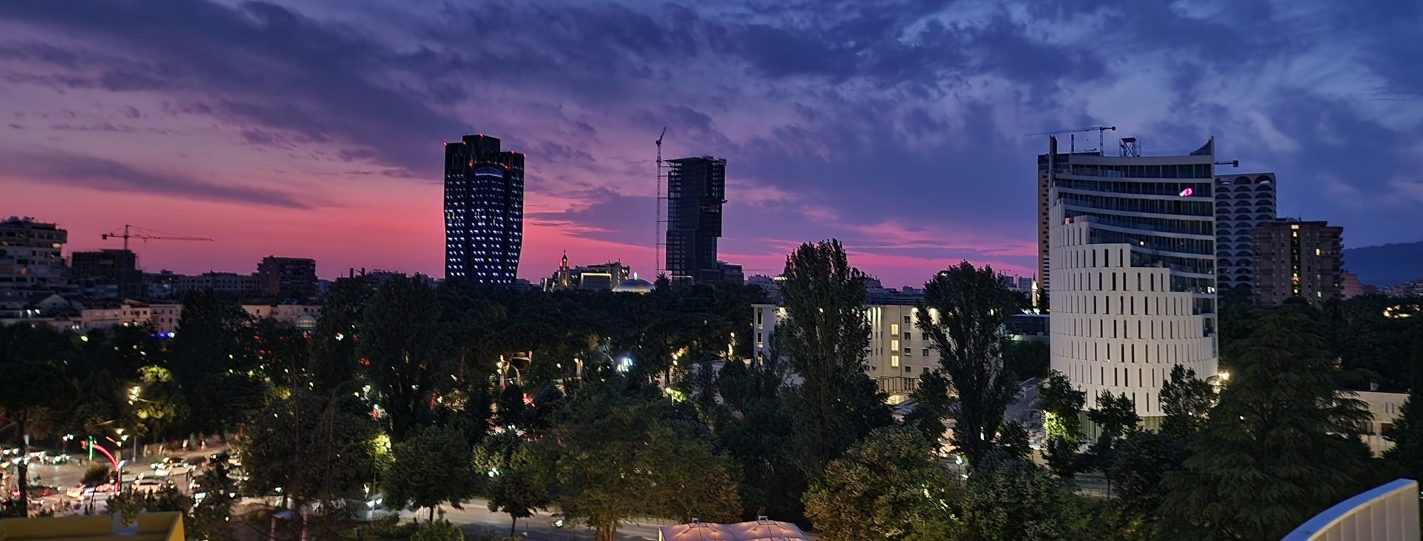 Tirana at night, lit apartment towers and street lights spreading across a valley under a dark sky.